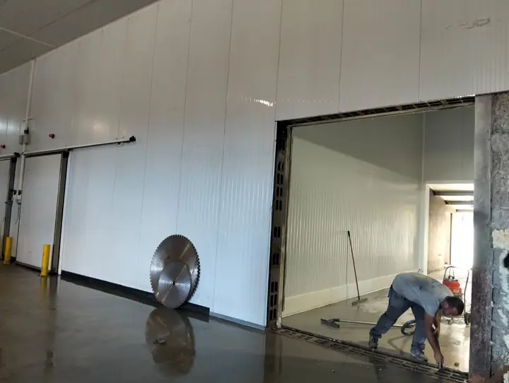 Abertura cortada na parede de uma câmara frigorífica, com o operador a limpar a base