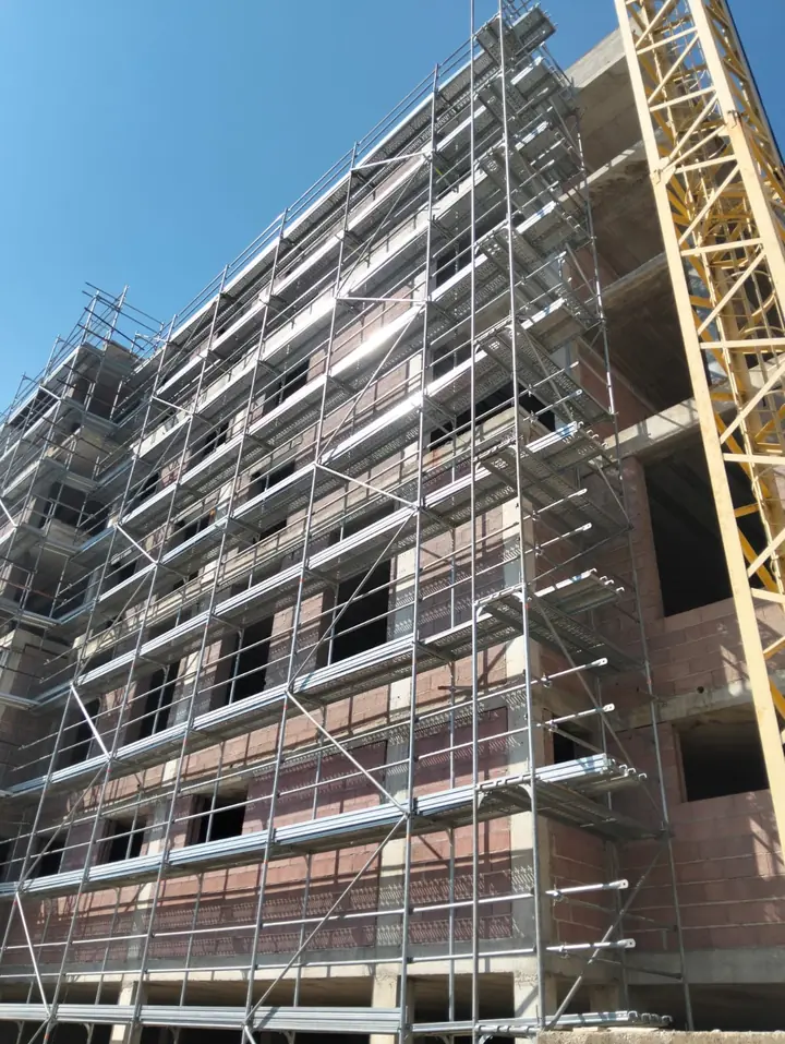 Andaime de fachada montado num edifício em construção, com grua ao lado