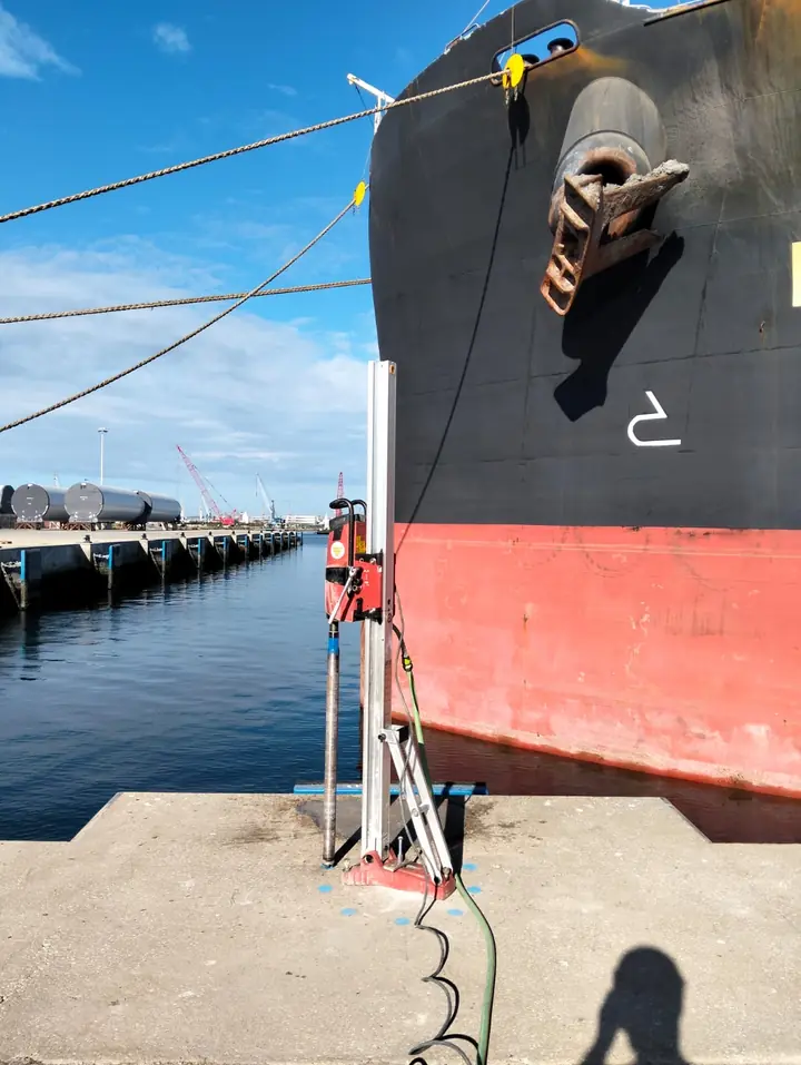 Caroteadora vertical no cais, ao lado da proa de um navio atracado
