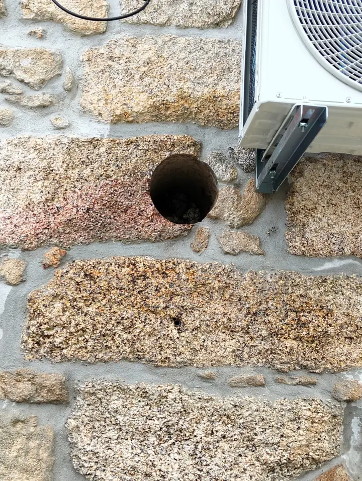 Furo redondo numa parede de granito junto à unidade exterior de ar condicionado