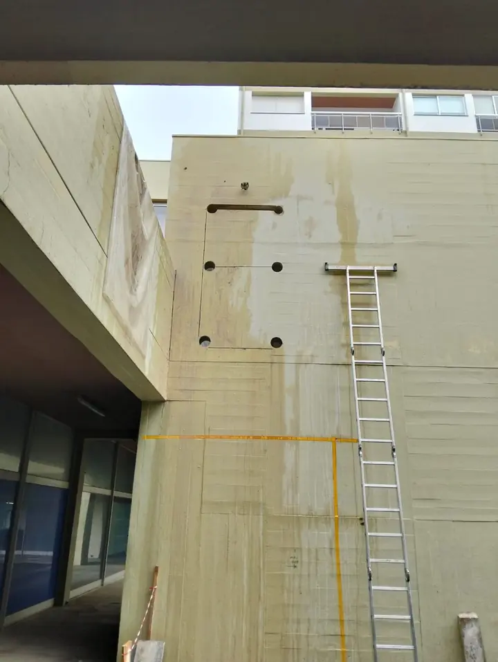 Fachada de betão com furos de passagem alinhados e escada de acesso